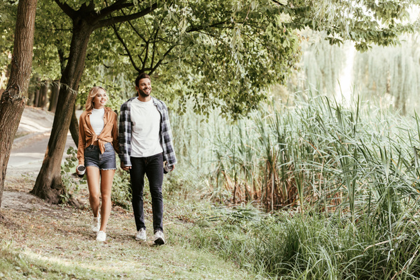 веселая молодая пара, держащаяся за руки во время прогулки по осеннему парку
 - Фото, изображение