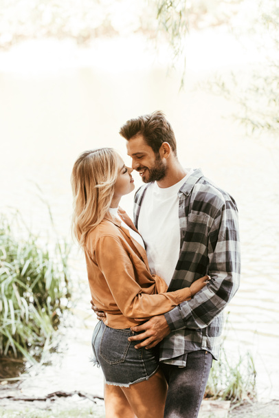 happy young couple smiling and hugging near lake in park - 写真・画像