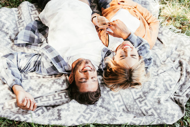 overhead view of cheerful young couple smiling while lying on blanket in park - Foto, afbeelding