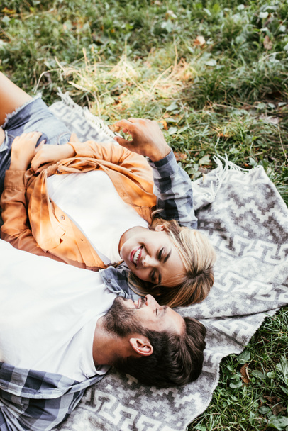 vue aérienne d'un jeune couple joyeux qui se regarde tout en étant allongé sur une couverture dans le parc
 - Photo, image