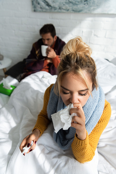 ill woman holding nasal spray and napkins in bedroom with man behind - Foto, Bild