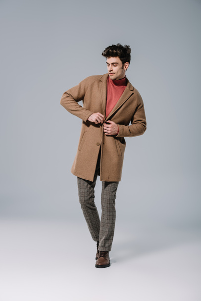 fashionable man posing in beige autumn coat on grey - 写真・画像