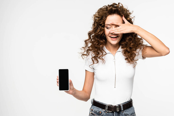 beautiful curly girl showing smartphone with blank screen, isolated on white - Фото, изображение