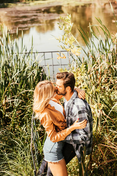 happy young couple embracing and kissing in thicket of sedge near lake - Photo, Image