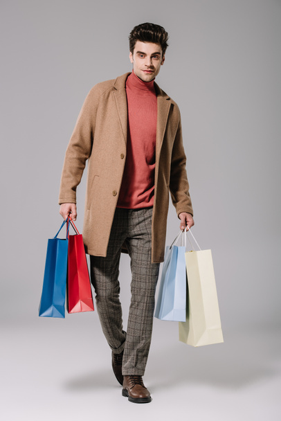 stylish man in beige coat holding shopping bags on grey - Photo, Image