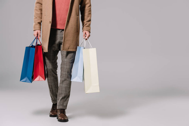 vista cortada de homem elegante em casaco bege segurando sacos de compras em cinza
 - Foto, Imagem