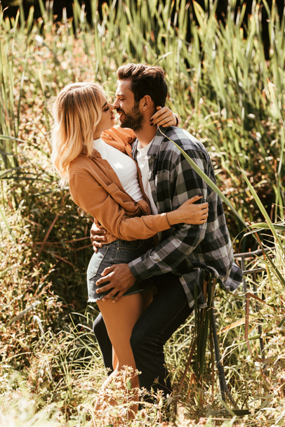 happy young couple embracing and kissing in thicket of sedge in park - Fotoğraf, Görsel