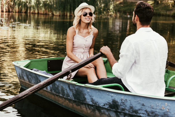 uśmiechnięta dziewczyna w sukience i okularach przeciwsłonecznych patrząc na chłopaka łodzi  - Zdjęcie, obraz