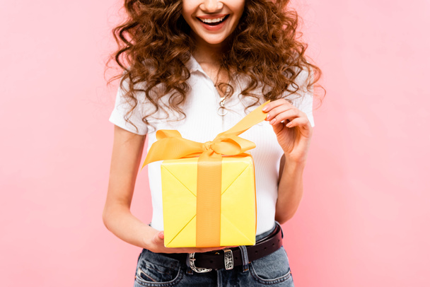 vista recortada de la feliz chica rizada sosteniendo caja de regalo, aislado en rosa
 - Foto, imagen
