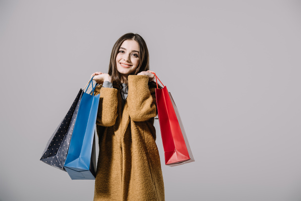 stylisches lächelndes Mädchen im beigen Mantel mit Einkaufstaschen, isoliert auf grau - Foto, Bild