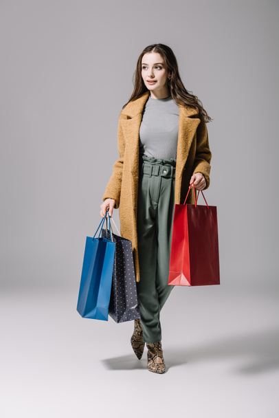 fashionable elegant woman in beige coat holding shopping bags on grey - Foto, afbeelding