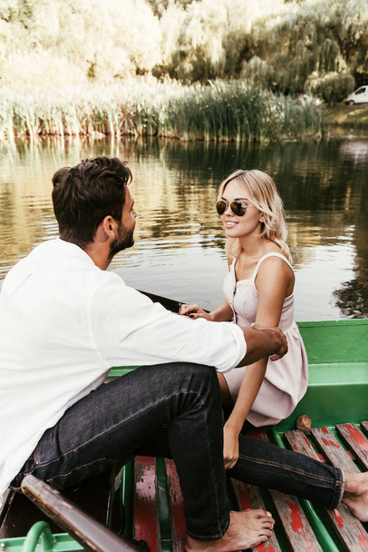 attractive, smiling woman looking at boyfriend while sitting in boat on lake - Foto, immagini