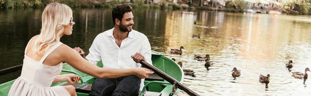 panoramic shot of young couple in boat on lake near flock of ducks - Photo, Image