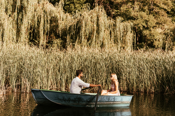 pareja joven en barco en el río cerca de matorral de junco
 - Foto, Imagen
