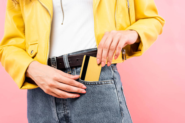 cropped view of girl putting credit card into pocket, isolated on pink - Foto, afbeelding