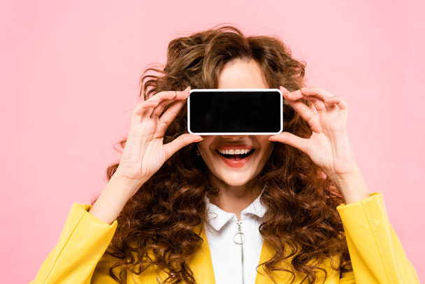 niña sonriente sosteniendo teléfono inteligente con pantalla en blanco en frente de la cara, aislado en rosa
 - Foto, Imagen