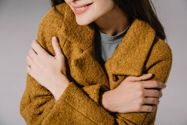 cropped view of smiling girl posing in warm beige coat, isolated on grey - Photo, image