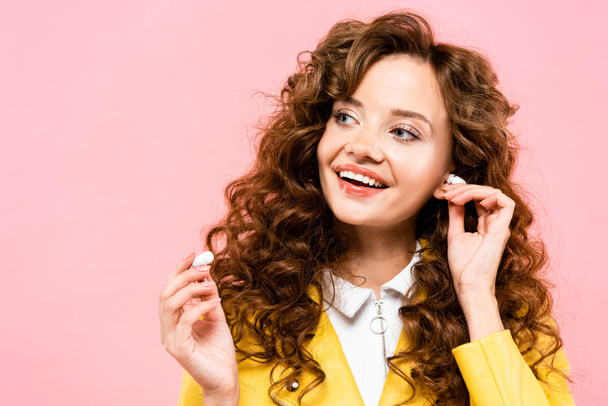 beautiful curly girl listening music with wireless earphones, isolated on pink - Photo, Image