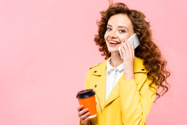 happy curly girl with coffee to go talking on smartphone, isolated on pink - Фото, изображение