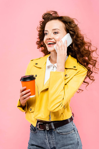 curly girl with coffee to go talking on smartphone, isolated on pink - Foto, imagen