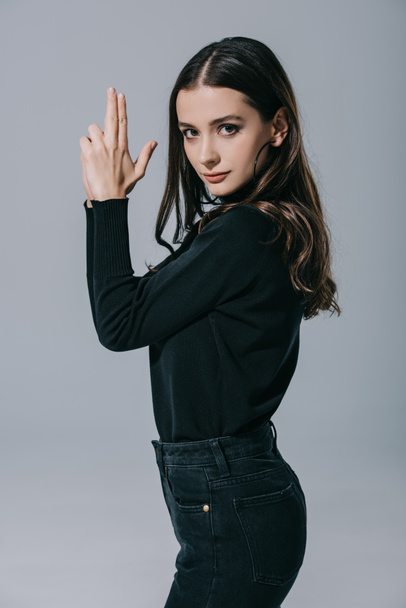 attractive fashionable girl in black sweater showing hand gun, isolated on grey - Fotó, kép