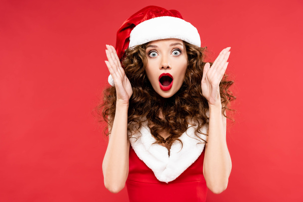 shocked girl gesturing and posing in santa costume, isolated on red - Foto, Bild