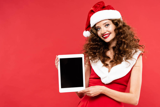 krásná dívka v kostýmu Santa ukazuje digitální tablet s prázdnou obrazovkou, izolované na červené - Fotografie, Obrázek