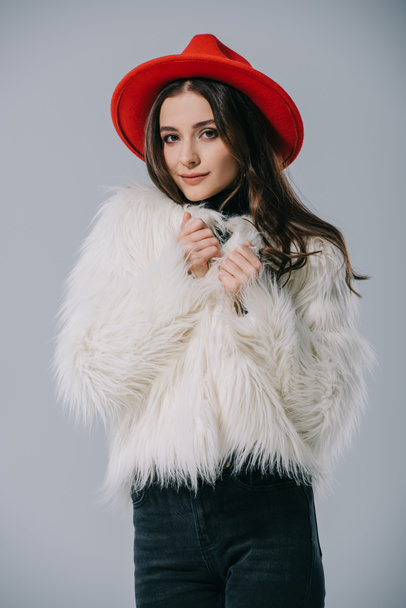 piękny elegancki model w białym futrze i czerwonym kapeluszu, odizolowany na szaro - Zdjęcie, obraz