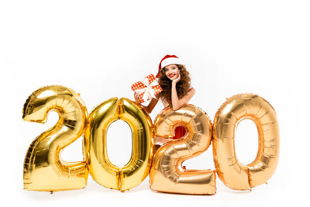 fille heureuse en costume de Père Noël tenant boîte cadeau tout en posant avec des ballons dorés 2020 nouvelle année, isolé sur blanc
 - Photo, image