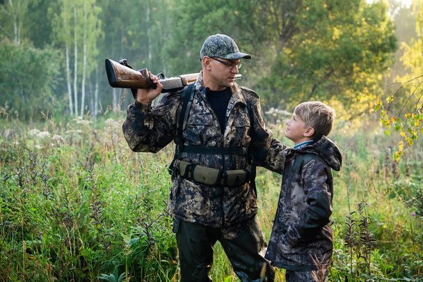 Padre con pistola che mostra qualcosa al figlio mentre caccia su una natura
. - Foto, immagini