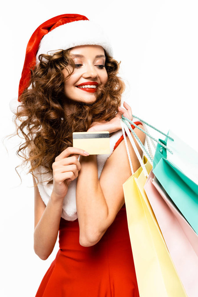 beautiful smiling girl in santa costume holding shopping bags and credit card, isolated on white - Фото, изображение