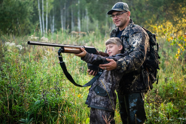 Vader leert zijn zoon over wapenveiligheid en het juiste gebruik van jagen in de natuur. - Foto, afbeelding