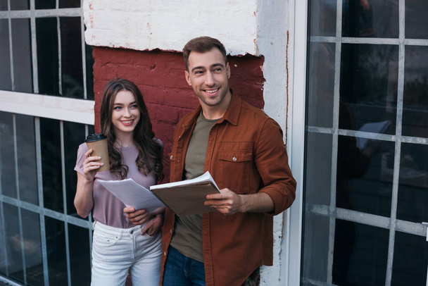cheerful businessman with documents and businesswoman with coffee to go looking away  - Photo, Image