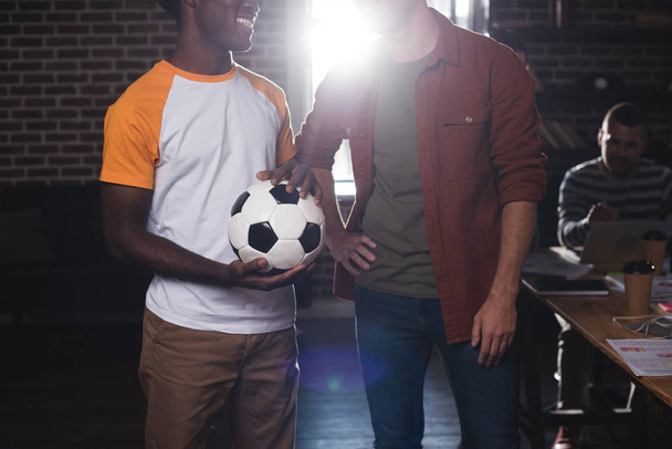 cropped view of african american businessman holding soccer ball near colleague standing with hand on hip - Fotoğraf, Görsel