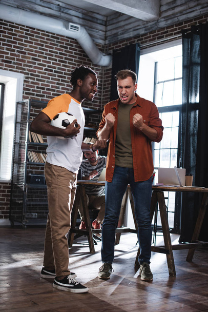 roztrzęsiony biznesmen gestykulujący podczas rozmowy z afrykańskim amerykańskim kolegą trzymającym kawę na wynos - Zdjęcie, obraz