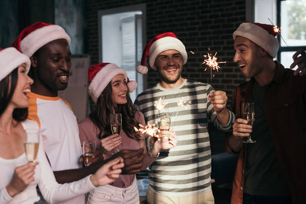happy, young businesspeople in santa hats holding sparklers and champagne glasses - Zdjęcie, obraz