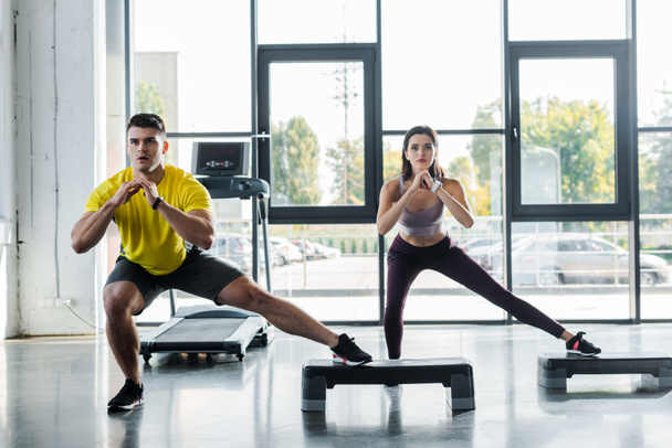 handsome sportsman and sportswoman doing lunges on step platforms in sports center - Foto, Imagen