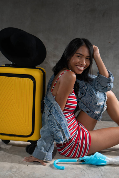 Portrét usmívající se mladé asijské ženy se zavazadly izolovanými přes betonovou stěnu. Životní styl lidí, cestování - Fotografie, Obrázek