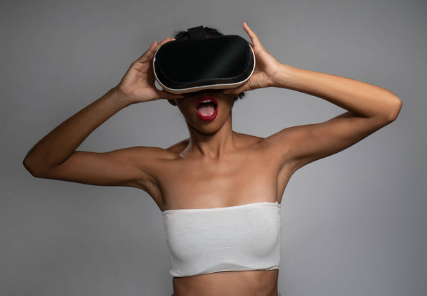 hübsche junge asiatische Mädchen posiert mit Virtual-Reality-Headset oder 3D-Brille isoliert über grauem Wandhintergrund - Foto, Bild