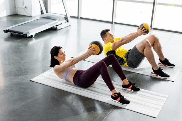 sportsman and sportswoman doing crunches with balls on fitness mats in sports center - 写真・画像