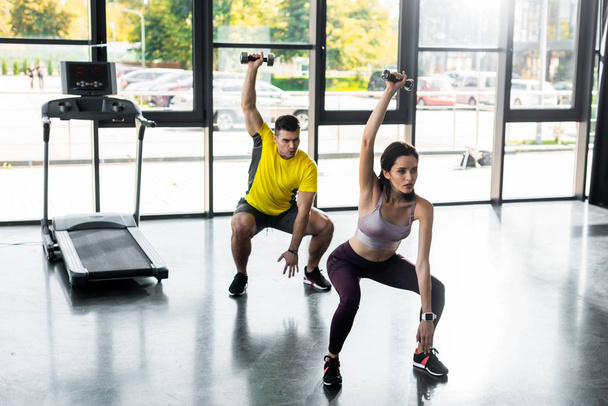 sportsman and sportswoman doing squat with dumbbells in sports center - Foto, afbeelding