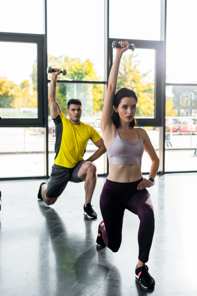 sportsman and sportswoman doing lunges with dumbbells in sports center - Foto, afbeelding