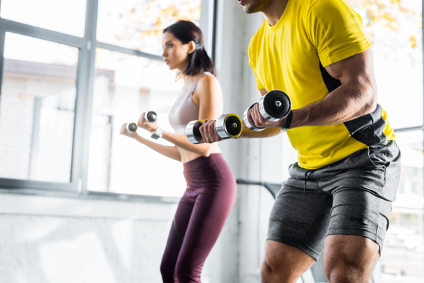 cropped view of sportsman and sportswoman working out with dumbbells in sports center - Photo, Image