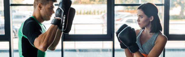 panoramic shot of sportswoman in boxing gloves working out with sportsman in sports center - Photo, Image