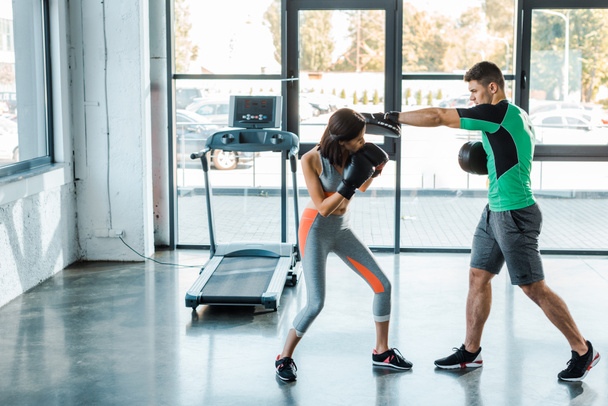 sportswoman in boxing gloves working out with sportsman in sports center - Photo, Image