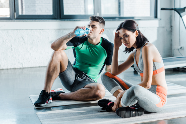 sportsman drinking water and sportswoman sitting in sports center - Photo, Image