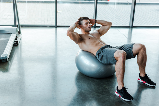 handsome sportsman doing crunches on fitness ball in sports center  - Zdjęcie, obraz