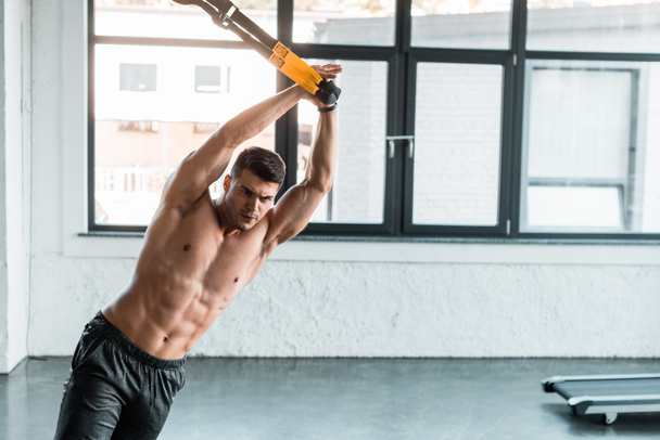 handsome sportsman working out on suspension trainer in sports center  - Photo, Image