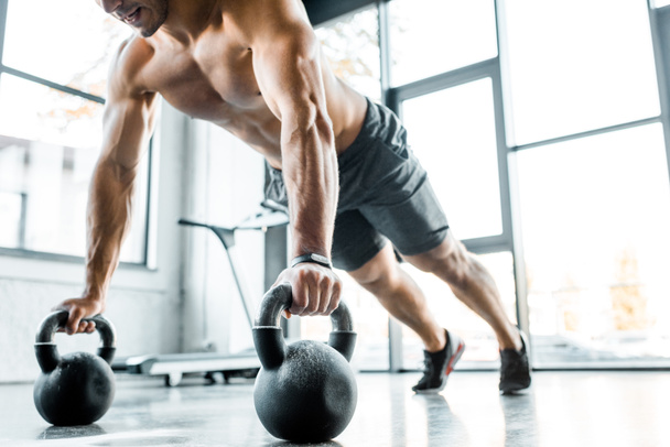 bijgesneden beeld van sporter doen push-ups op gewichten in sportcentrum  - Foto, afbeelding
