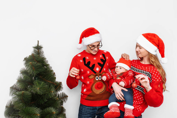 Happy family in Christmas hats, mom dad and little child celebrate Christmas and decorate the Christmas tree. - Foto, Bild